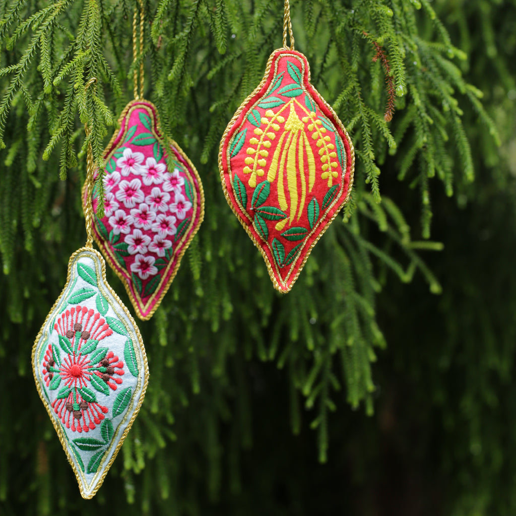 Colourful embroidered Christmas tree decorations hanging in from the branches of a tree.