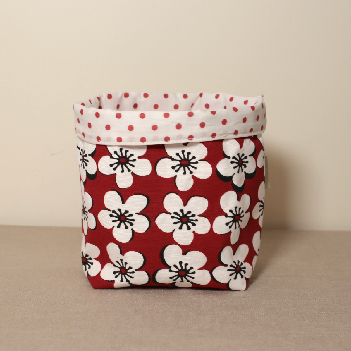 A red fabric pot with a floral pattern and a white polka dot rim on top.