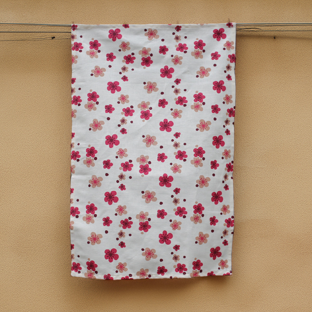 A pink flower printed hemp tea towel handing next to a honey coloured concrete wall.