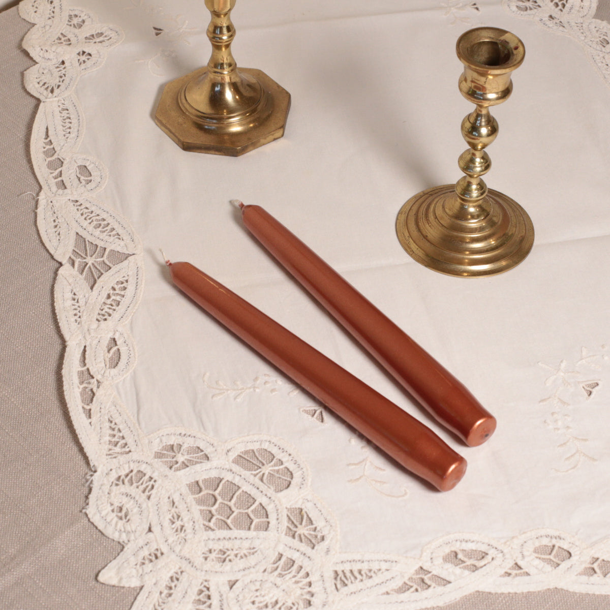 Two tapered Venetian-style copper table candles on a lace tablecloth.