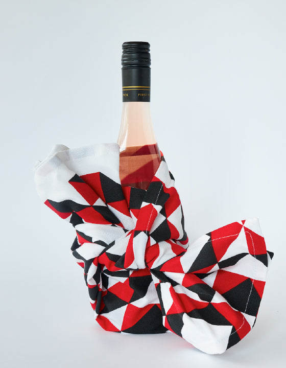 A wrapped wine bottle with a red, black and white geometric tea towel.