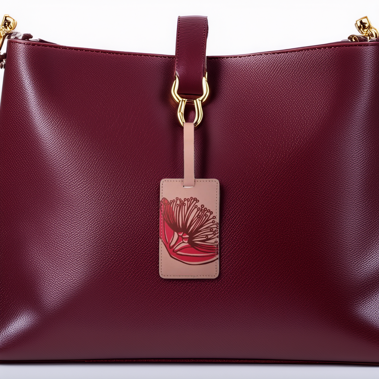 A magenta leather luggage tag with a Pohutukawa design, attached to a luggage bag.