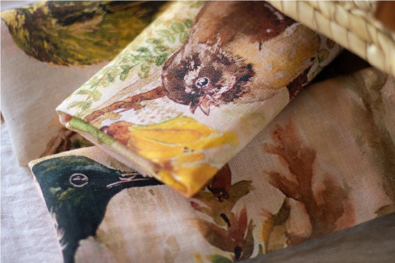 Close up of two natural coloured tea towels with New Zealand birds on them spilling out of a basket