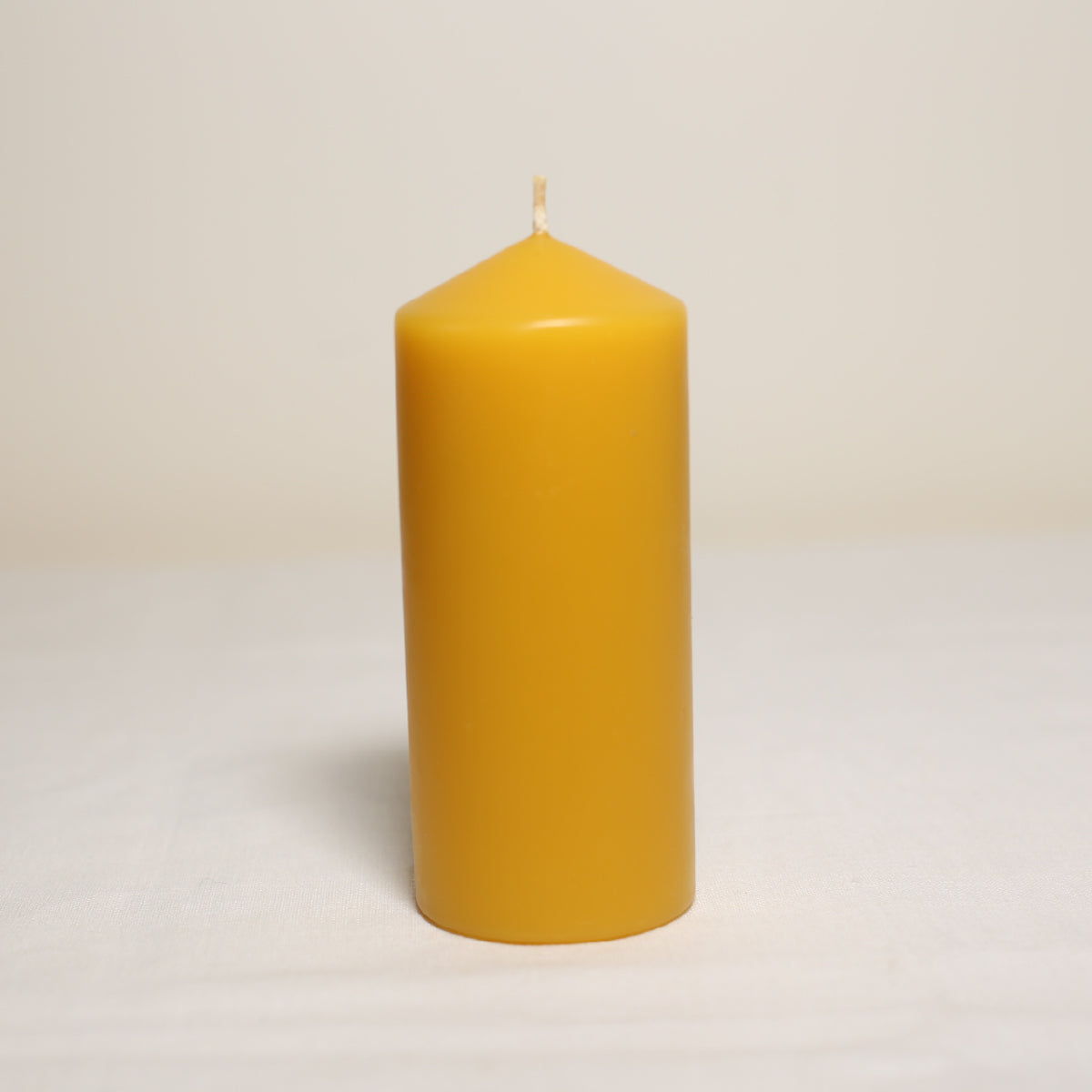 A single yellow beeswax pillar candle on a white background.