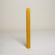 A single beeswax table candle on a plain background, showing a yellow candle with a lit wick.