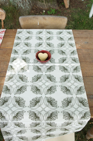 A table runner with a leaf pattern in olive green color displayed on a wooden table.