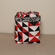 A fabric pot with a geometric pattern in red, black, and white colors, handcrafted from organic cotton.