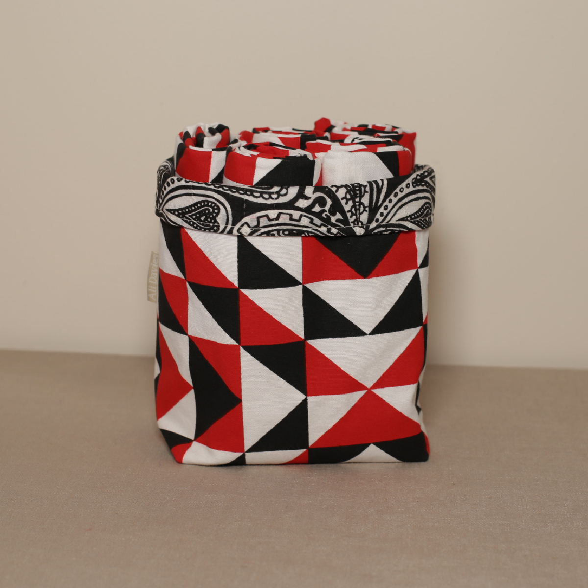 A fabric pot with a geometric pattern in red, black, and white colors, handcrafted from organic cotton.