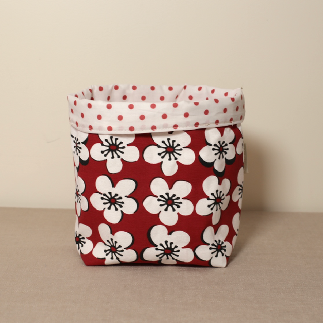A red fabric pot with a floral pattern and a white polka dot rim on top.