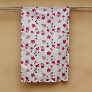 A pink flower printed hemp tea towel  handing next to a honey coloured concrete wall. 