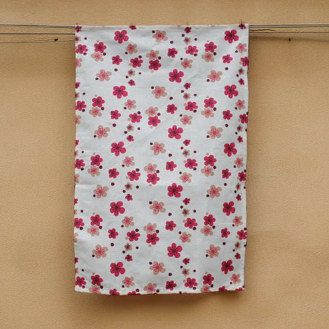 A pink flower printed hemp tea towel  handing next to a honey coloured concrete wall. 