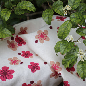 Closeup pink flowers printed fabric on a natural base with leaves of a trees resting on the fabric