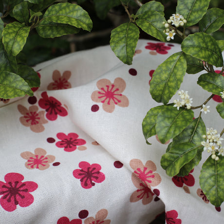 Closeup pink flowers printed fabric on a natural base with leaves of a trees resting on the fabric
