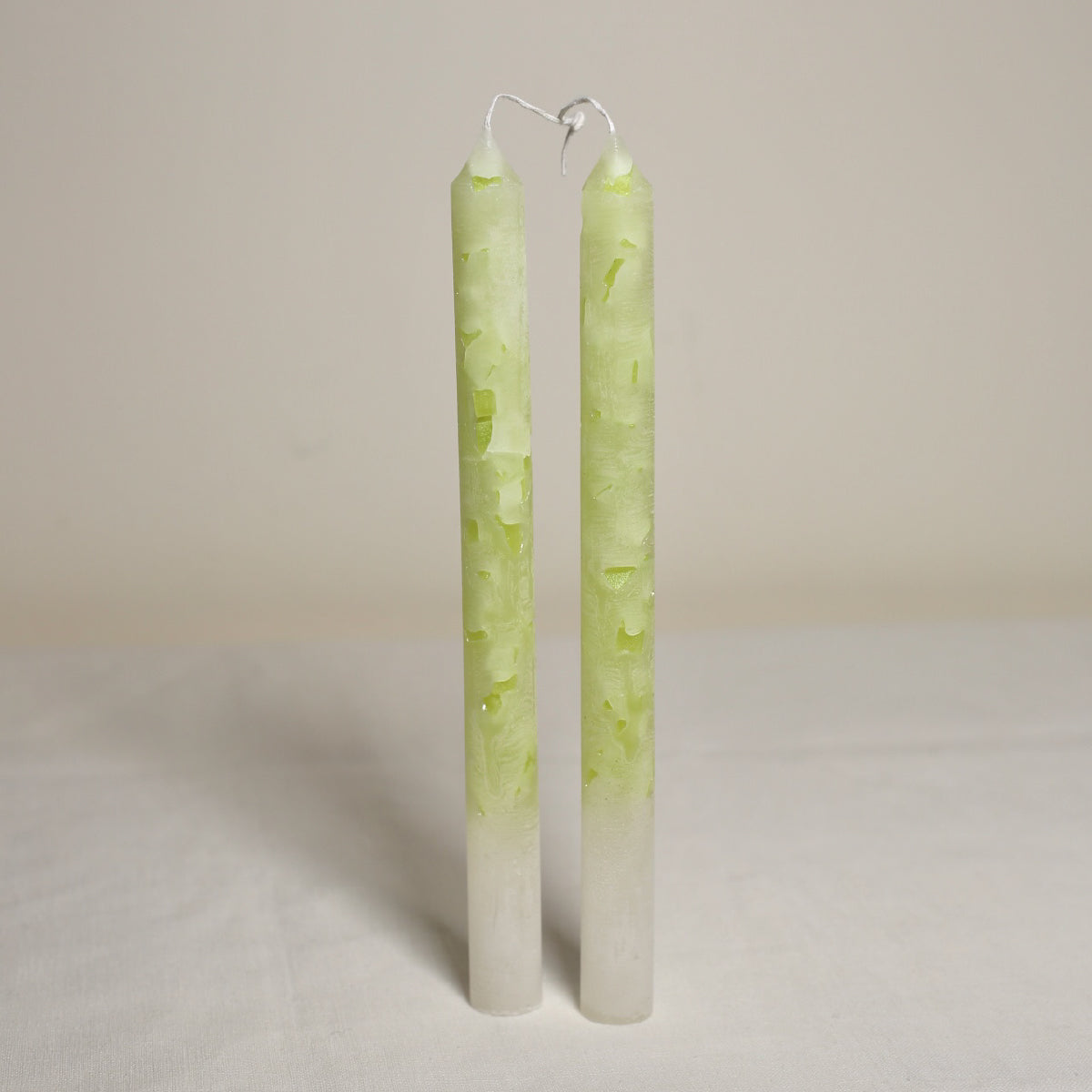 A pair of tall, marble effect, guava-colored table candles placed side by side on a light background.
