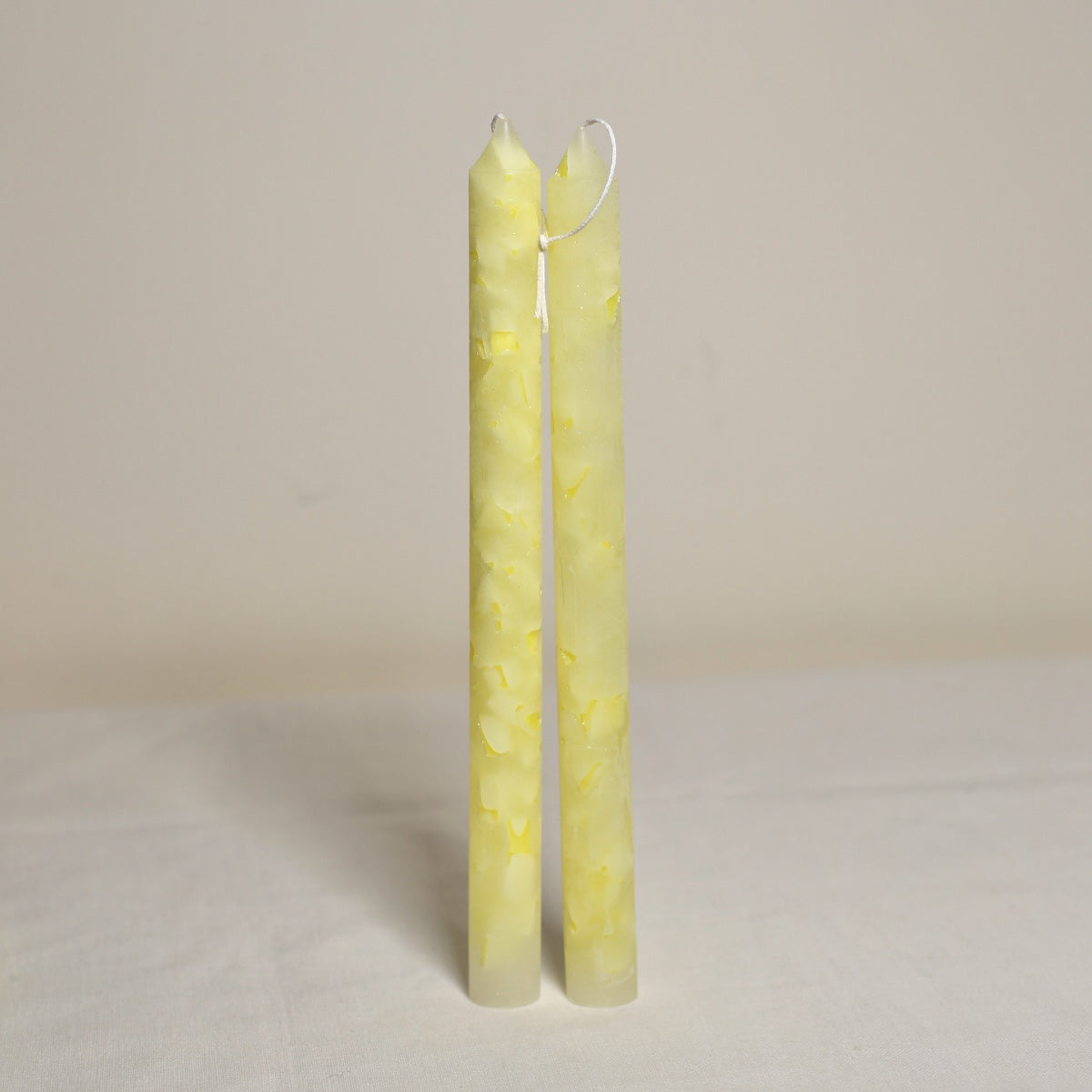 A pair of yellow marbled table candles placed upright on a surface with a light background.