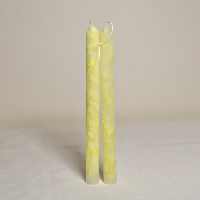 A pair of yellow marbled table candles placed upright on a surface with a light background.