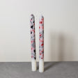 A pair of handmade marble effect table candles with white tops and a mix of black, gray, and red marbled patterns below.