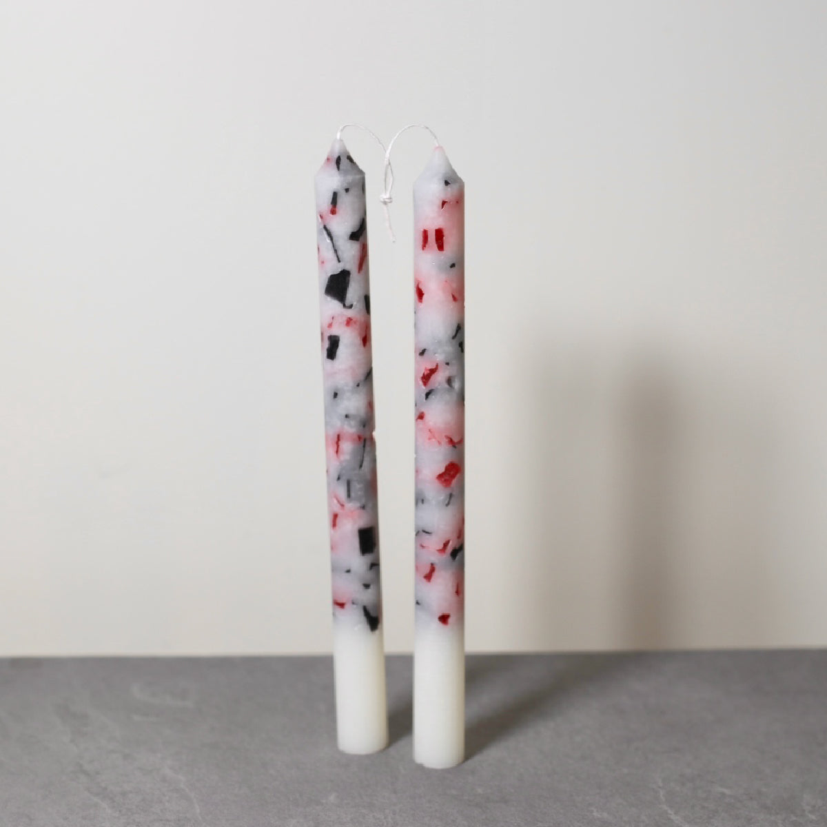 A pair of handmade marble effect table candles with white tops and a mix of black, gray, and red marbled patterns below.