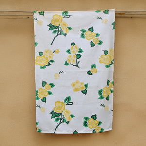 A white hemp tea towel with a green and yellow floral pattern, hanging on a wall.