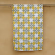 A hemp tea towel with a geometric Pacifica Kowhai pattern in olive green and Ceylon yellow, hanging on a yellow wall.