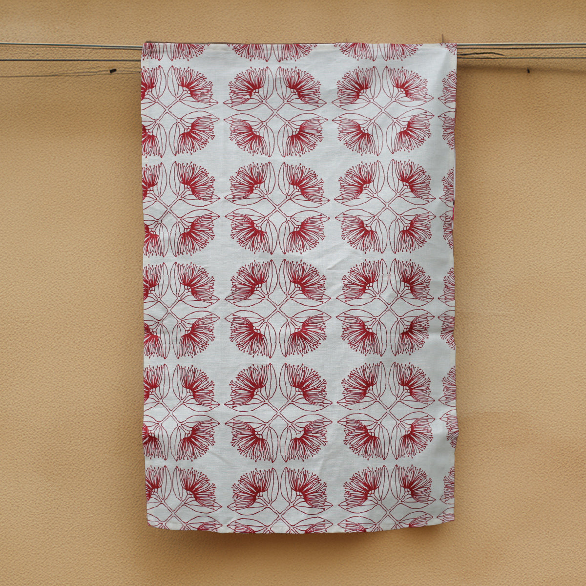 A hemp tea towel with a 'salsa' red pohutukawa print design, hanging on a wall.