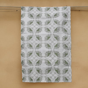 A white hemp tea towel with an olive green Pohutukawa flower print, hanging on a line against a beige wall.