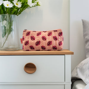 Small pink floral toilet bag sitting on a bedside table next to a vase of flowers.