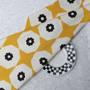 Closeup of yellow star and black flower printed hemp tea towel on a marble benchtop with black & white plate.