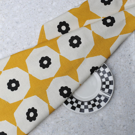 Closeup of yellow star and black flower printed hemp tea towel on a marble benchtop with black & white plate.