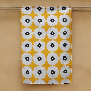 A yellow star and black flower printed hemp tea towel  handing next to a honey coloured concrete wall. 