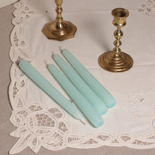 A pair of aqua tapered Venetian-style table candles on a lace doily.