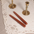 Two tapered Venetian-style copper table candles on a lace tablecloth.