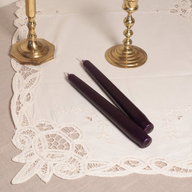 A pair of purple tapered Venetian-style table candles on a lace doily.