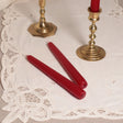 A pair of red tapered Venetian-style table candles on a lace doily.