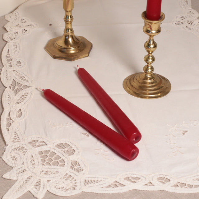 A pair of red tapered Venetian-style table candles on a lace doily.