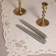 A pair of silver tapered Venetian-style table candles on a lace doily.
