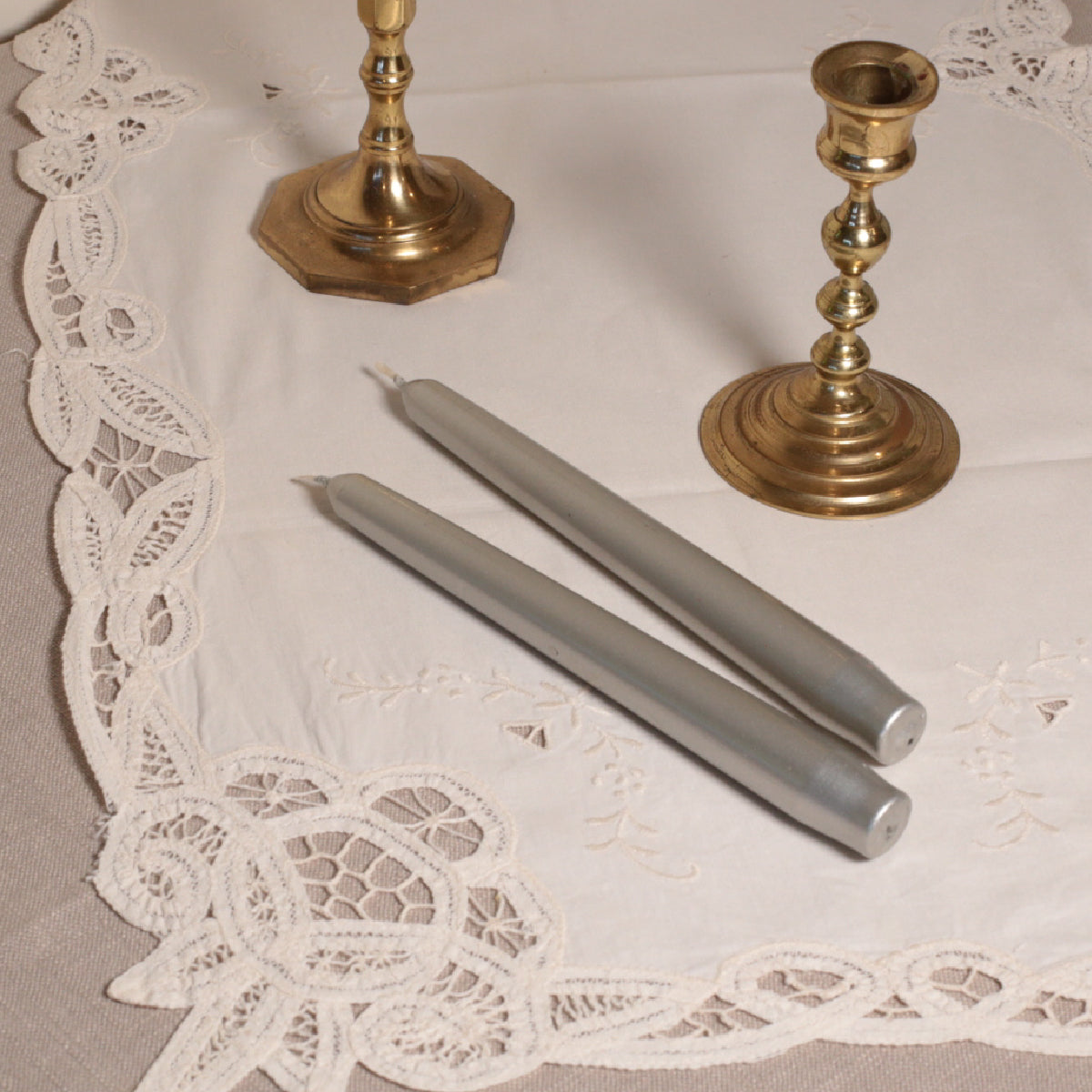 A pair of silver tapered Venetian-style table candles on a lace doily.