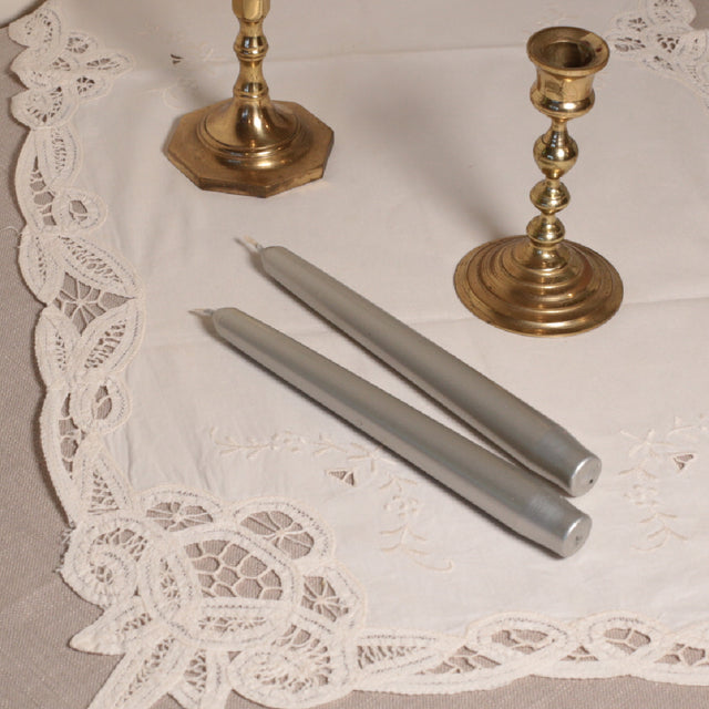 A pair of silver tapered Venetian-style table candles on a lace doily.