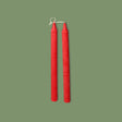 A pair of handmade ribbed table candles in Venetian Red color, displayed vertically against a green background.