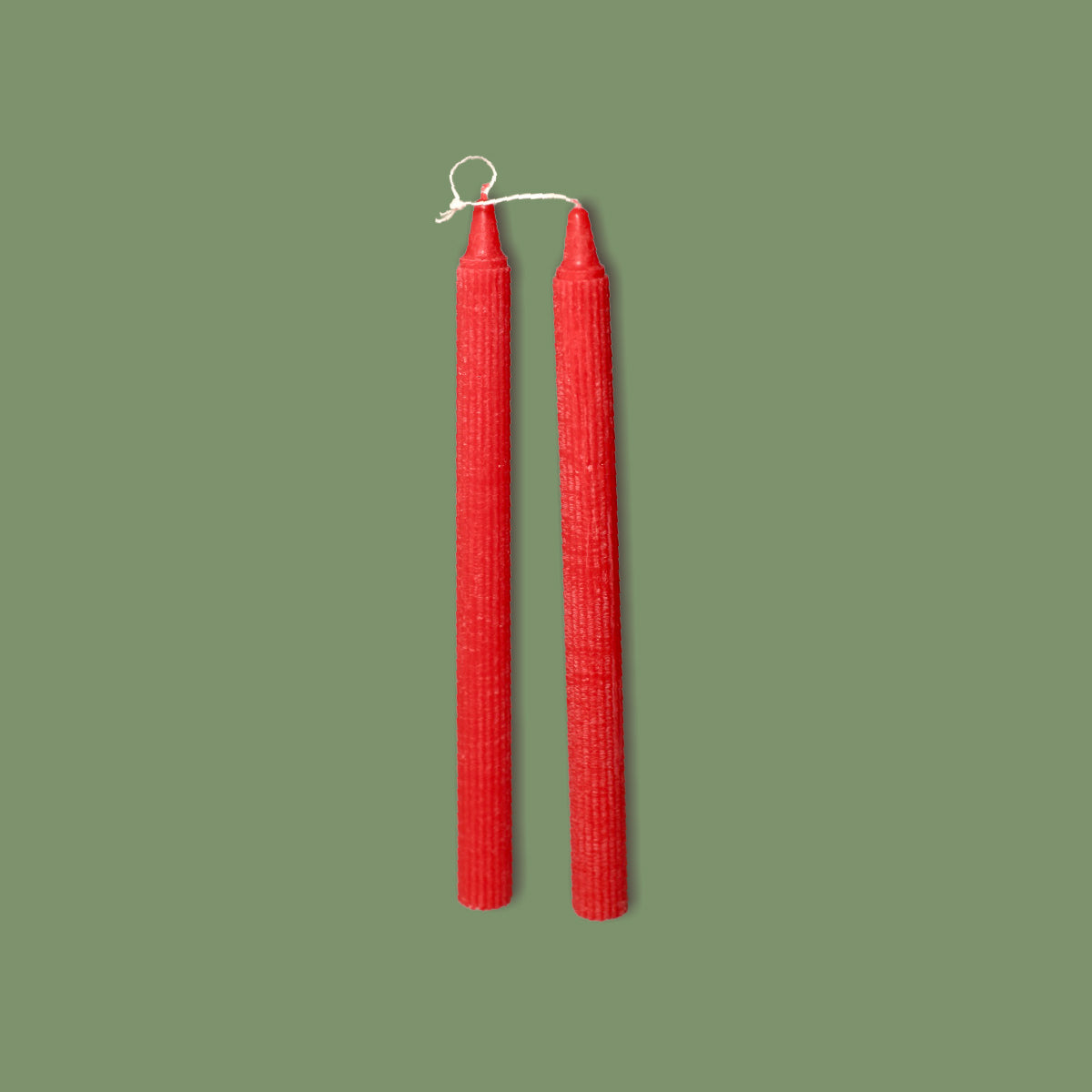 A pair of handmade ribbed table candles in Venetian Red color, displayed vertically against a green background.