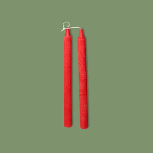 A pair of handmade ribbed table candles in Venetian Red color, displayed vertically against a green background.
