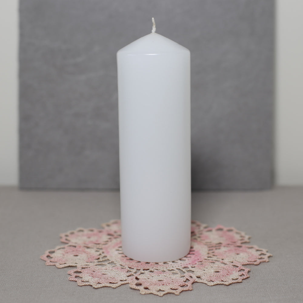 A white pillar candle on a pink lace doily with a grey background.