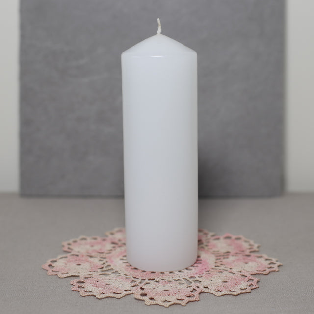 A white pillar candle on a pink lace doily with a grey background.
