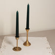 Two tapered Venetian-style table candles with green wax and gold-colored metal sticks, displayed on a lace tablecloth.