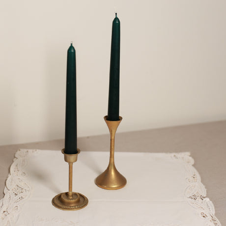 Two tapered Venetian-style table candles with green wax and gold-colored metal sticks, displayed on a lace tablecloth.
