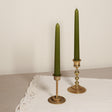 Two tapered Venetian-style olive green candles with gold-colored bases on a lace tablecloth.