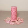 A pink patterned pillar candle on a pink lace doily.