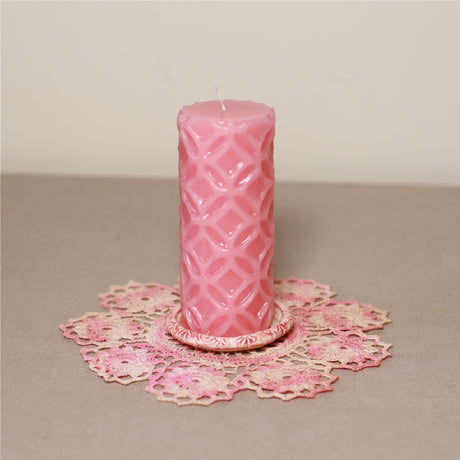 A pink patterned pillar candle on a pink lace doily.
