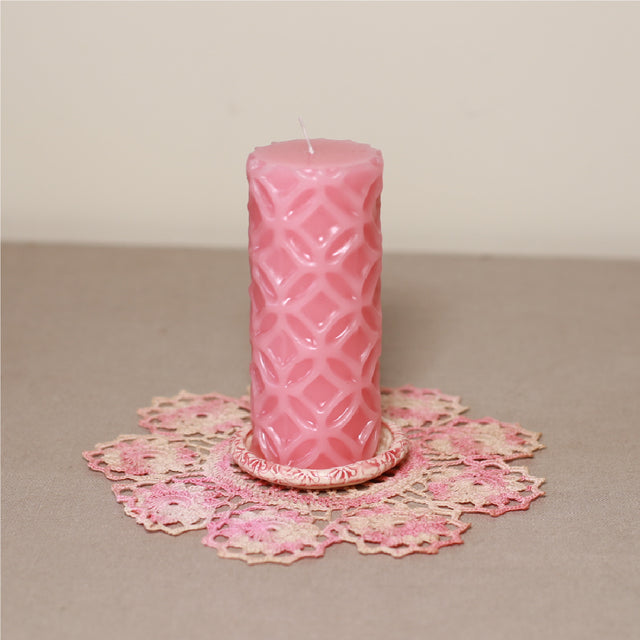 A pink patterned pillar candle on a pink lace doily.