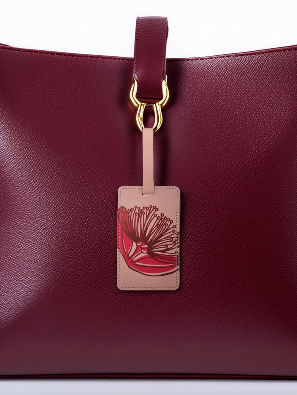 A magenta leather luggage tag with a Pohutukawa design, attached to a luggage bag.